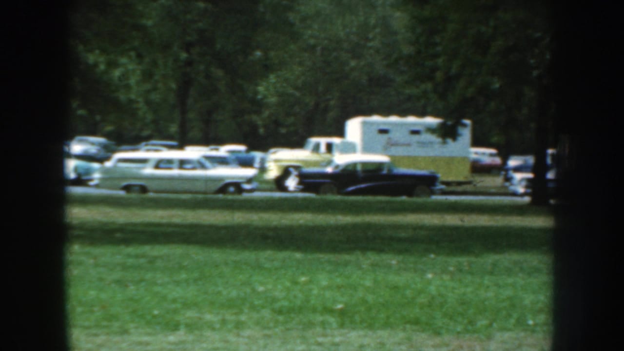 Line of parked cars with a white and yellow caravan trailer visible near the curb.