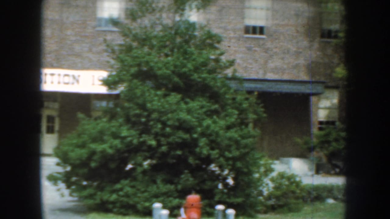 1959 Nebraska exterior view of the brick exposition building with trees obscuring part of the banner and a red fire hydrant near the lawn.