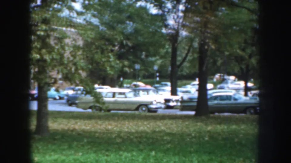 Late-1950s cars are parked beyond a tree-lined lawn during a quiet Nebraska home-movie pan.