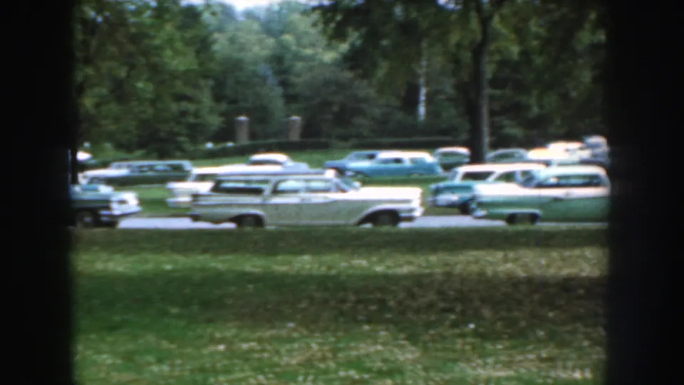 A row of 1950s cars in pale colors appears parked beside a wooded road in Nebraska home-movie footage.
