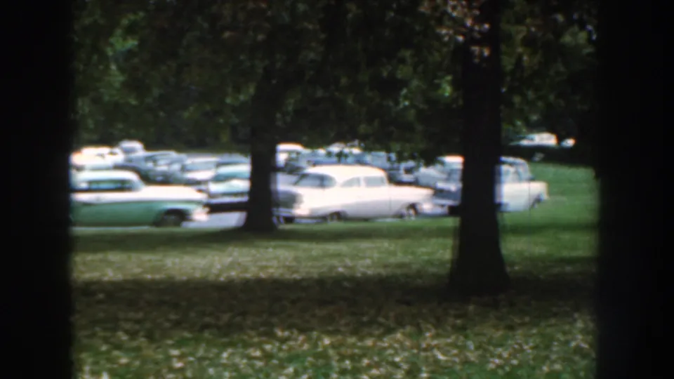 End frame of Nebraska 1959 footage showing parked 1950s cars through a dark foreground tree line.