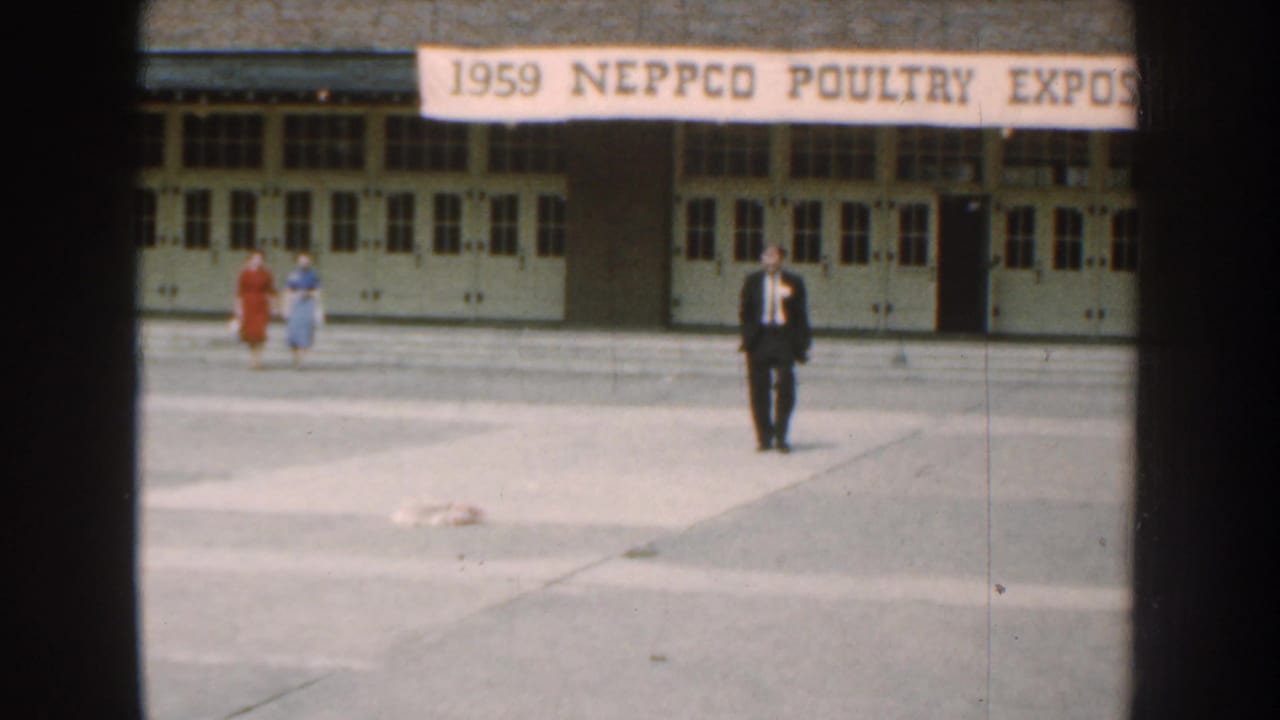 Two women and a suited man outside a building with a 1959 poultry expo banner.