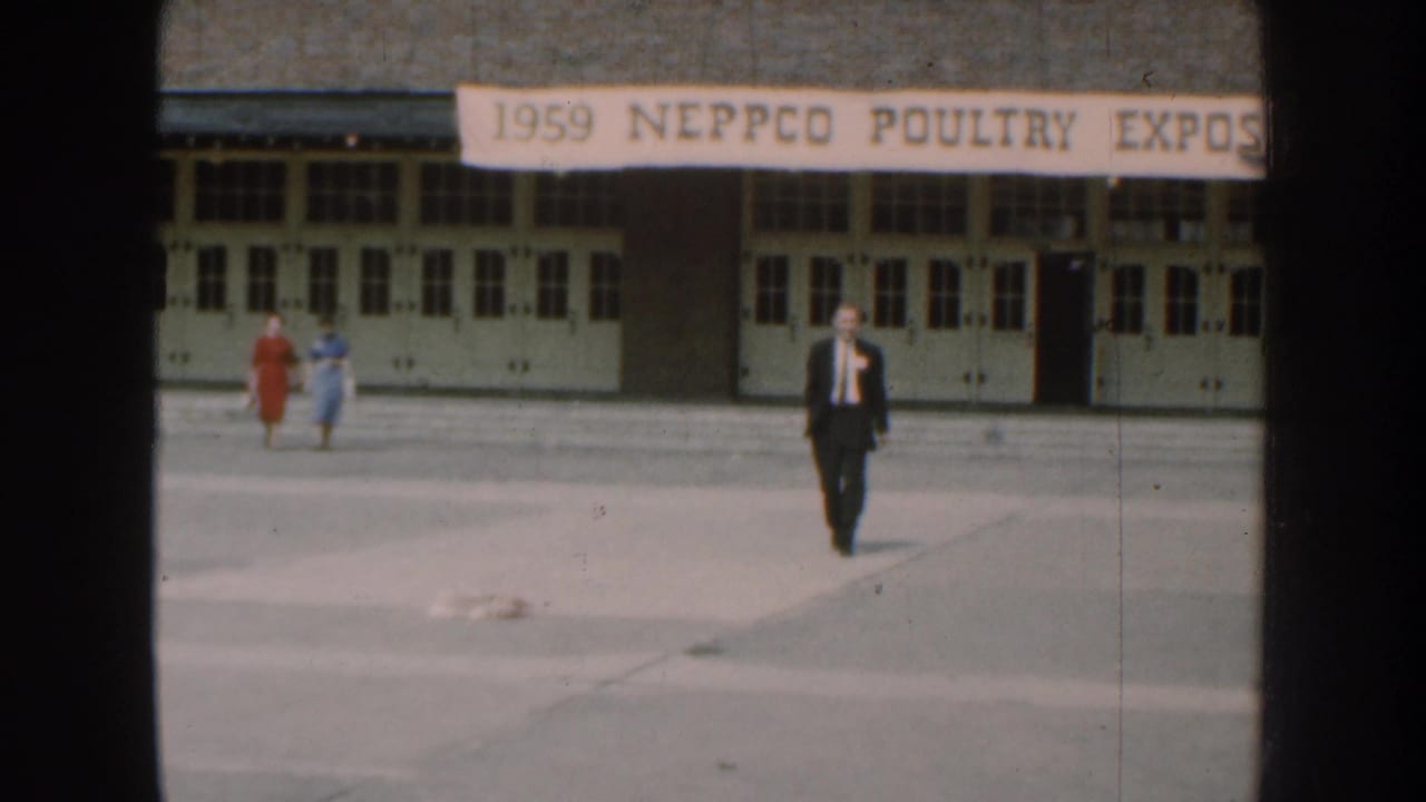 A suited man walks toward the camera while two women cross near the exhibition building.