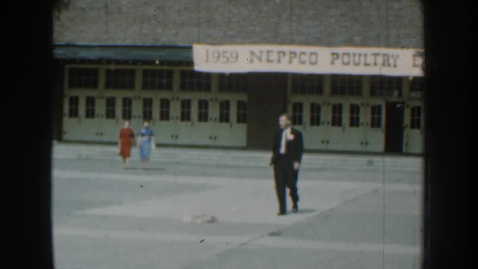 1959 Nebraska home-movie frame of a suited man and two women outside the NEPPCO Poultry Expo building.