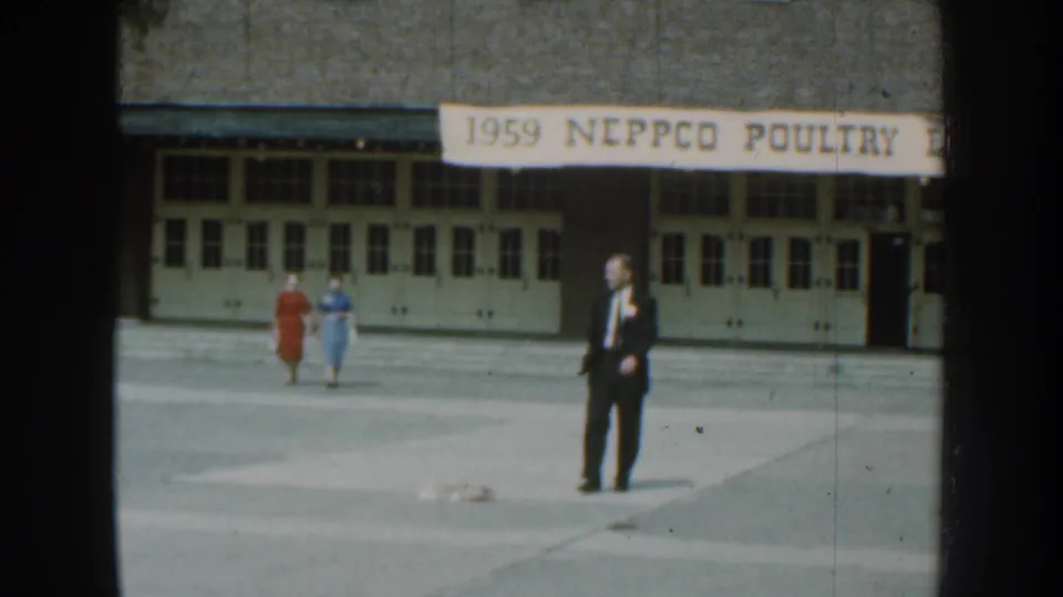In supported 1959 Nebraska footage, adults walk across a paved area outside a building marked by a NEPPCO Poultry banner.