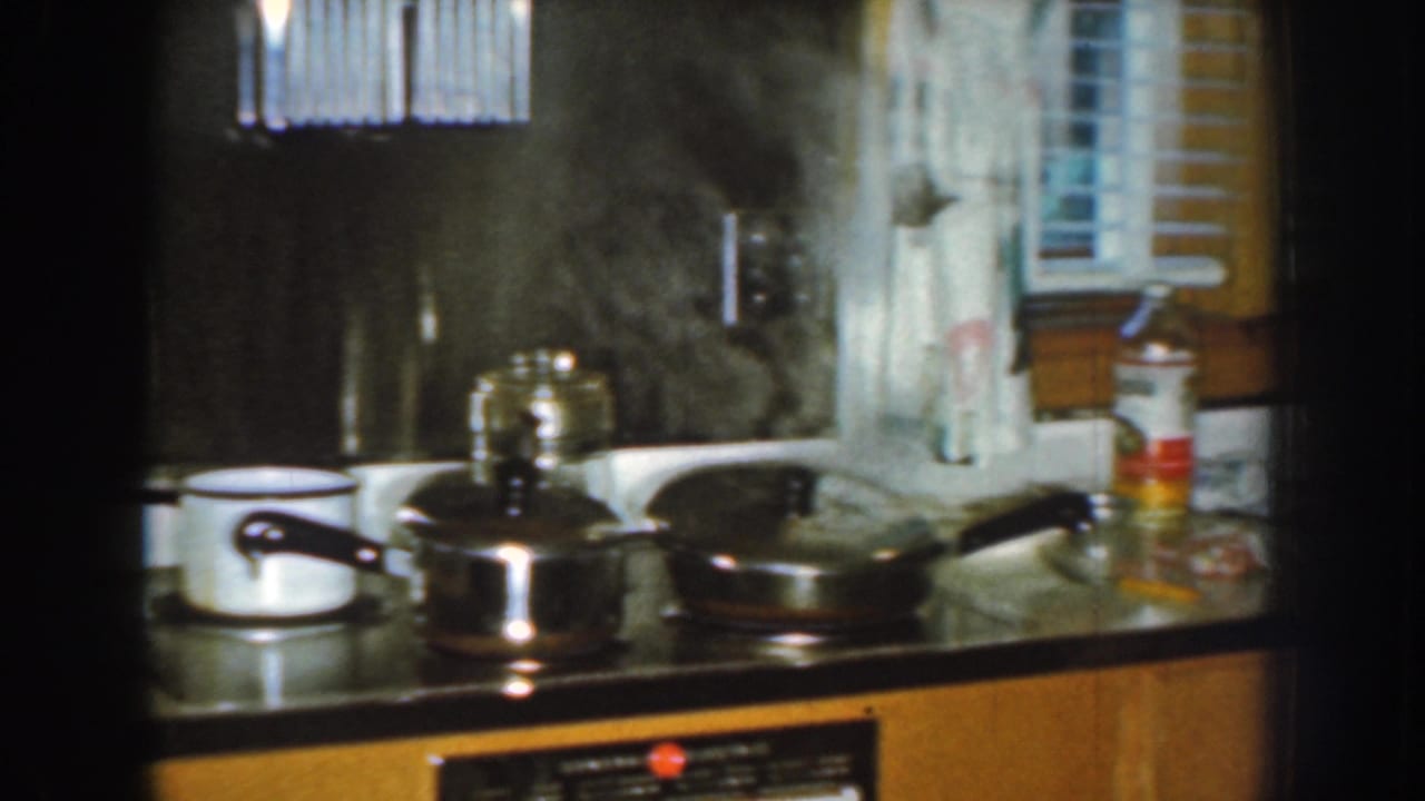 Stovetop and sink area with pots, a pan, steam, window blinds, and wood cabinets.