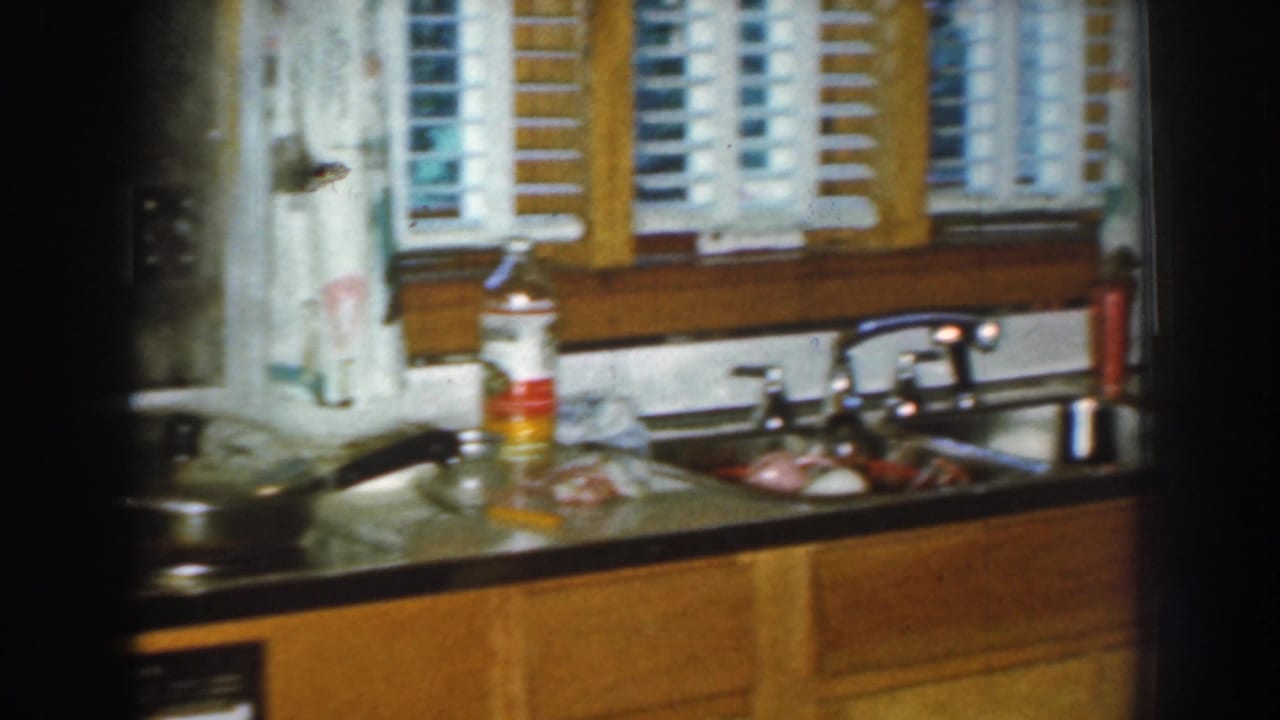 Kitchen counter with sink, faucet, cookware, dish items, window blinds, and wood cabinets.