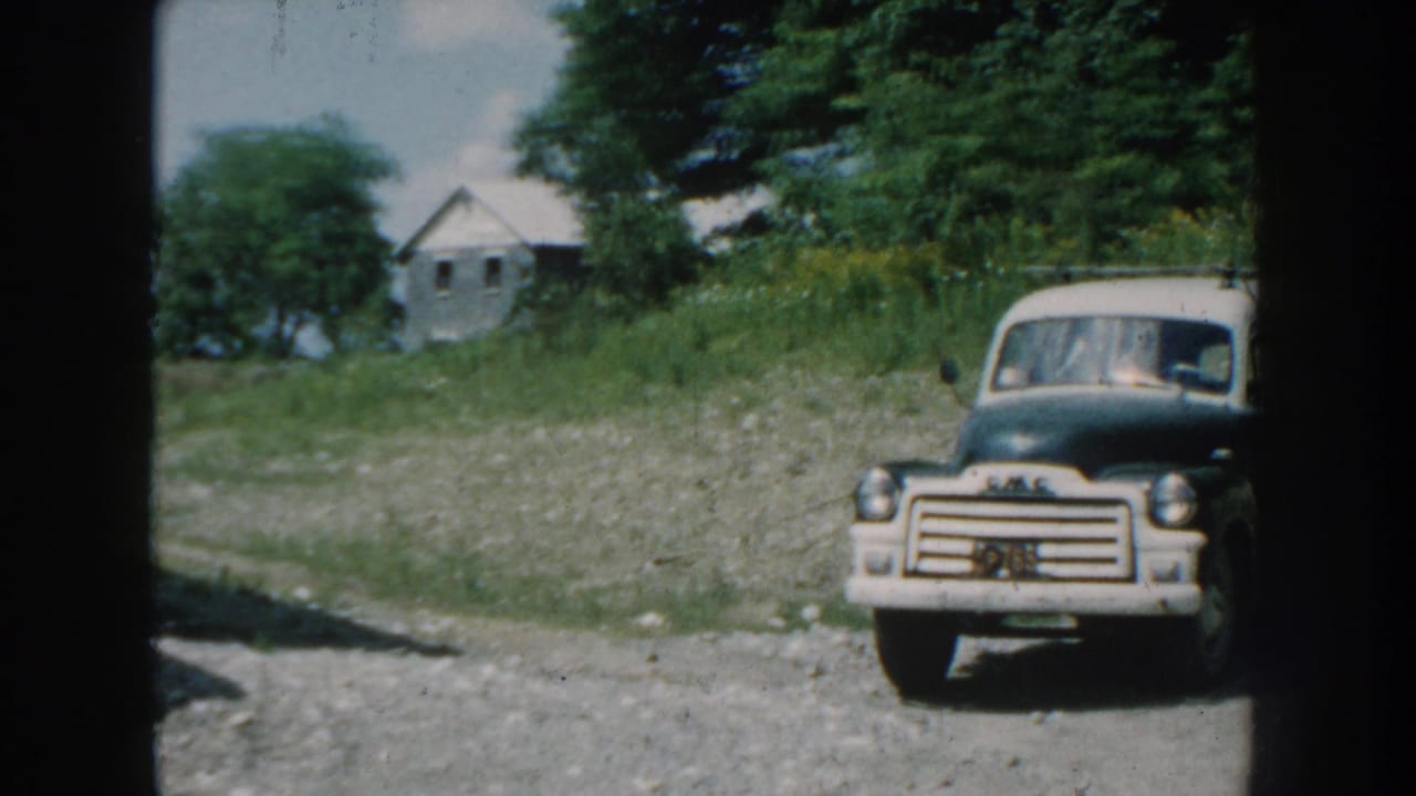GMC truck parked on a gravel lot with trees and a small house behind it.