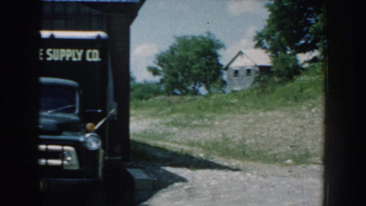 A dark Garden State Supply Co. delivery truck appears partly obscured beside a rural building in 1959 Nebraska footage.