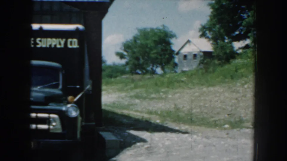 A dark Garden State Supply Co. delivery truck appears partly obscured beside a rural building in 1959 Nebraska footage.