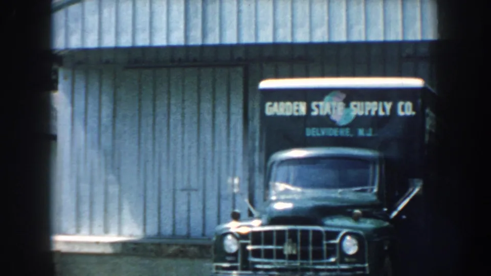 1959 Nebraska frame with a Garden State Supply Co truck front, partial second truck, and corrugated wall.