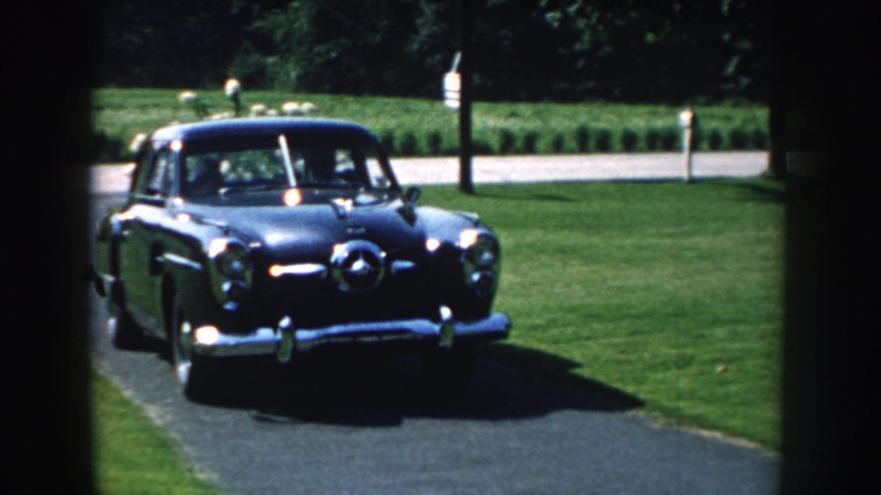 Dark blue sedan entering a paved driveway beside a green lawn.