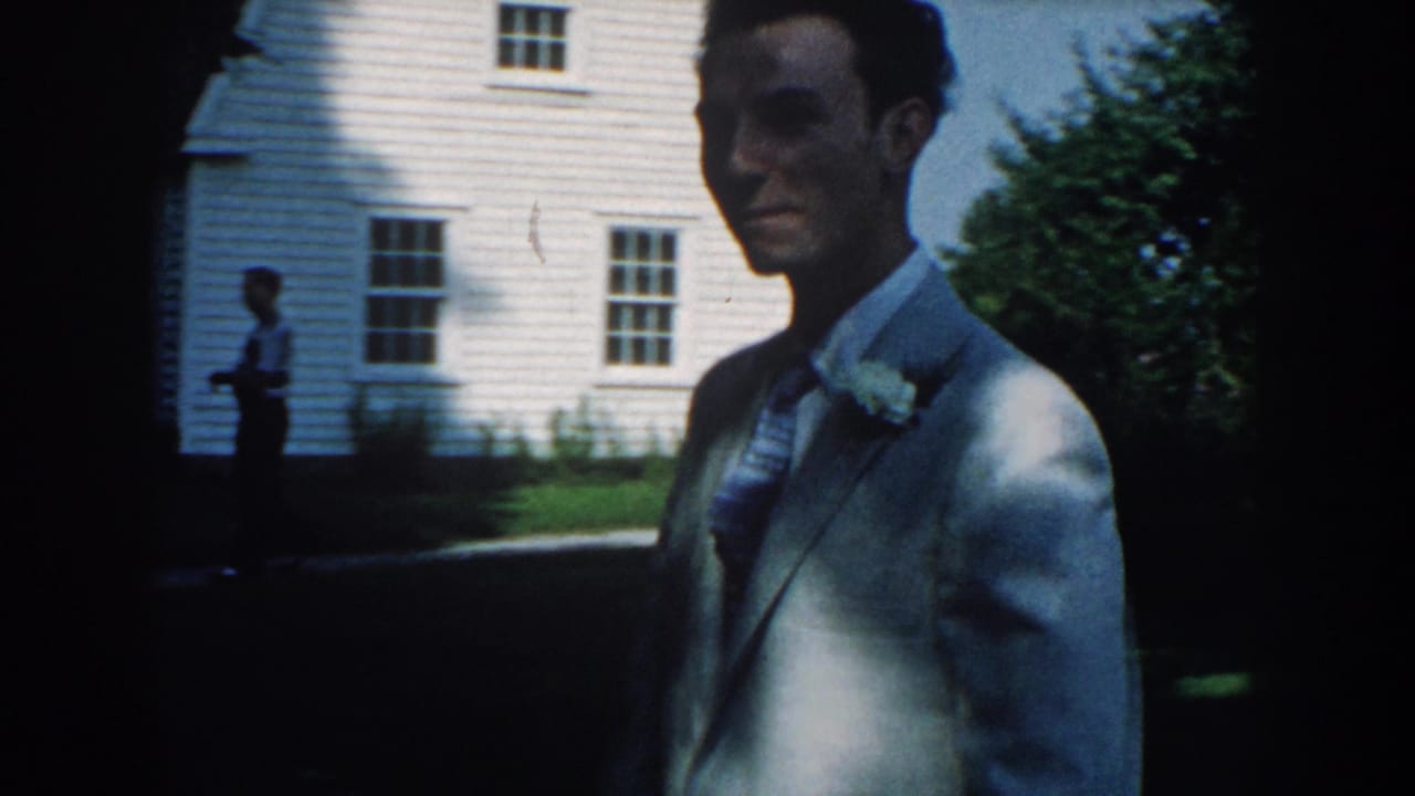 Man in a light suit walks past a white clapboard house.