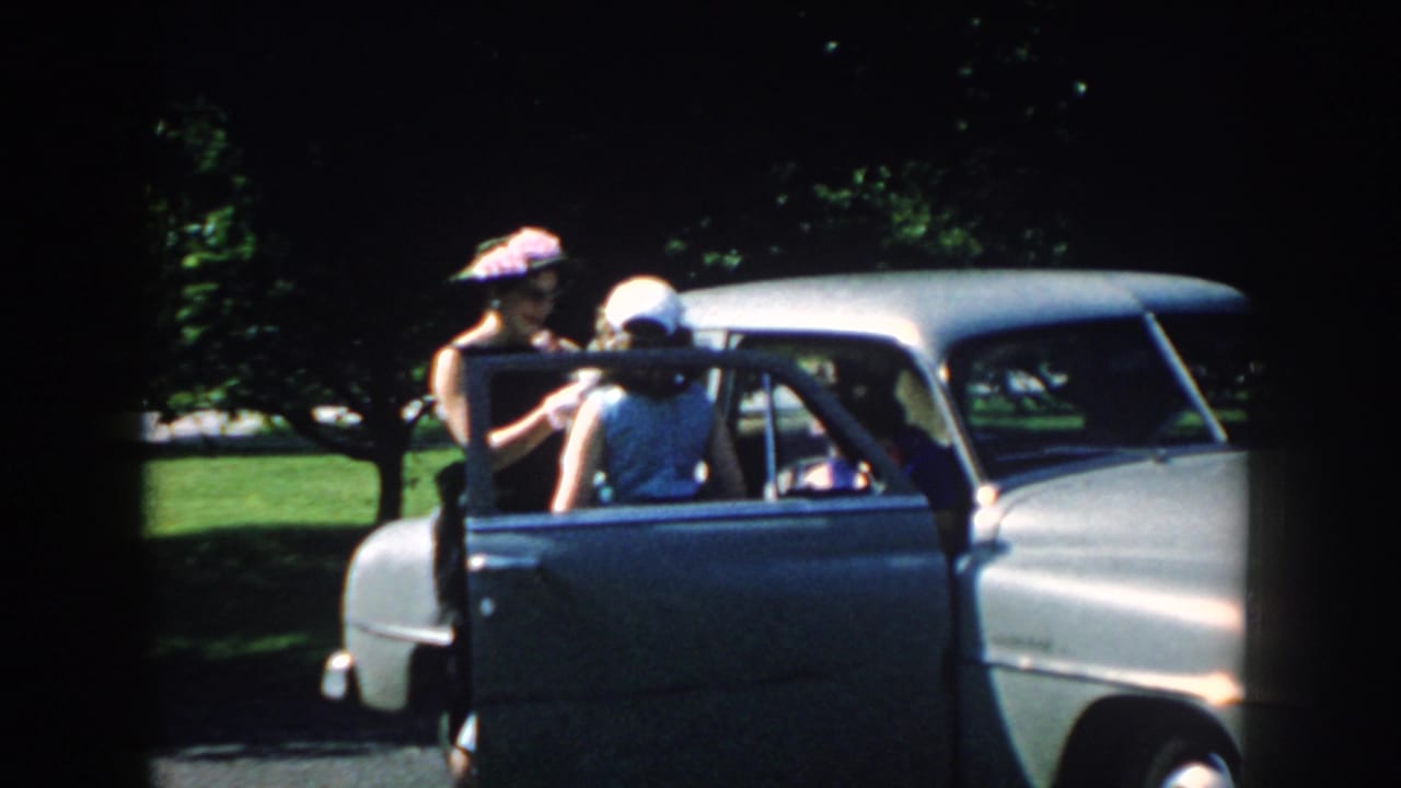 In 1959 Nebraska home-movie footage, women gather at an open door of a two-tone sedan in a sunny park.