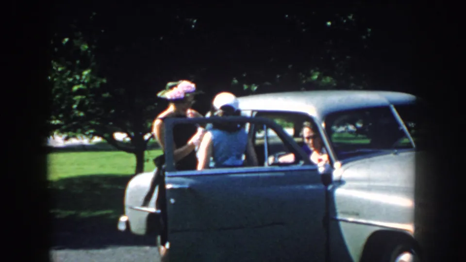 A woman in a floral hat stands by the open door as another woman faces into the car in this 1959 Nebraska park scene.