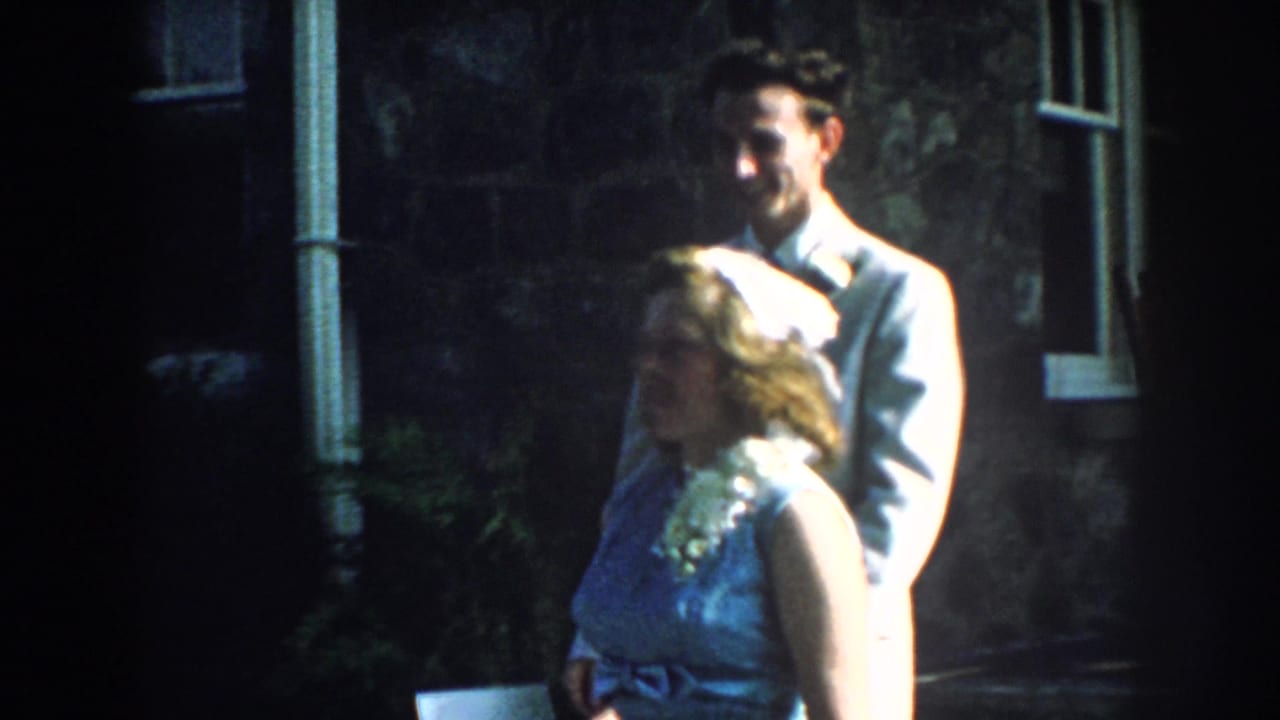 Couple in formal attire outside a stone house with white-paned windows.