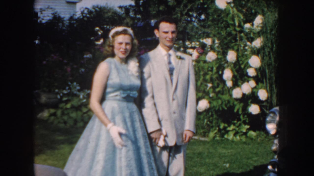 Young woman and man standing together in front of white flowering bushes.