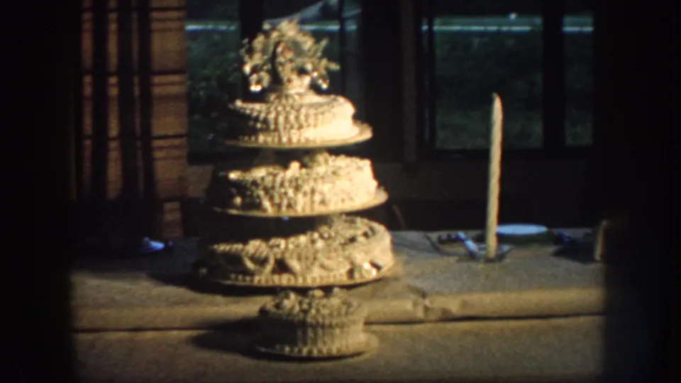 Close view of a decorated three-tier wedding cake displayed indoors or on a sheltered table in 1959 Nebraska footage.