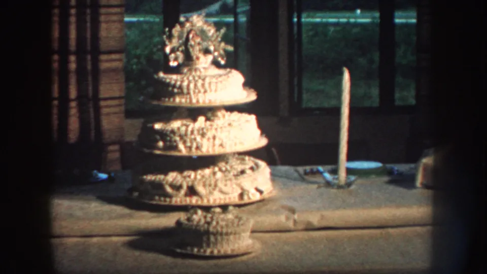 The home movie lingers on the tiered wedding cake, with icing details, tableware, and window light visible.