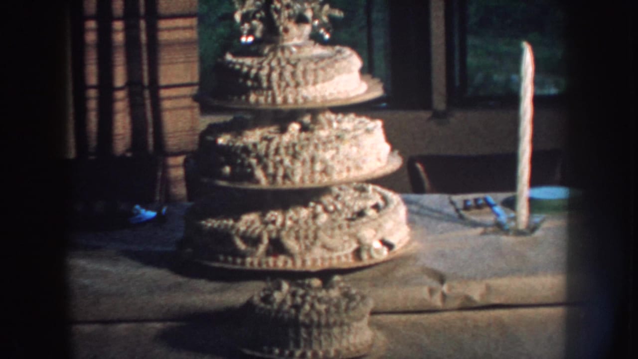 White wedding cake and tall candle on a table with windows behind them.