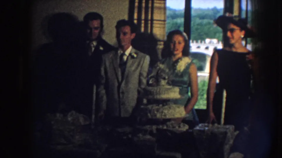 Nebraska 1959 wedding reception view with suited guests, a woman in green, and a foreground silhouette near the cake.