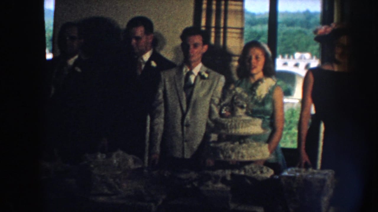Wedding party poses near the cake table with a woman in a hat at the edge of the group.