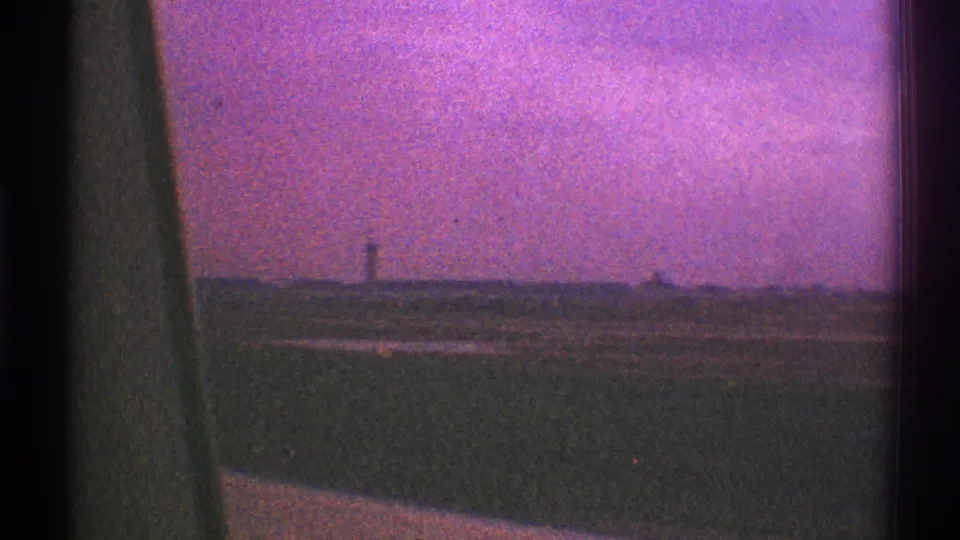 Side-looking 8mm frame from a moving vehicle in Los Angeles, with dark window trim, open roadside, distant tower shape, and magenta sky.
