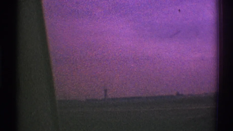Color-shifted 1969 8mm frame showing a low roadside horizon and sky through a moving vehicle window in Los Angeles.