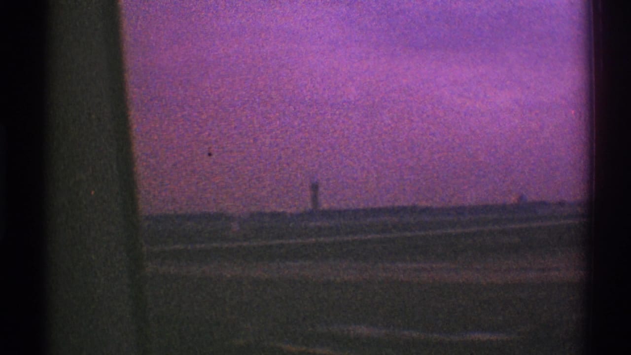 1969 Los Angeles airport runway area seen from an airplane window, with a distant control tower and magenta-shifted sky.