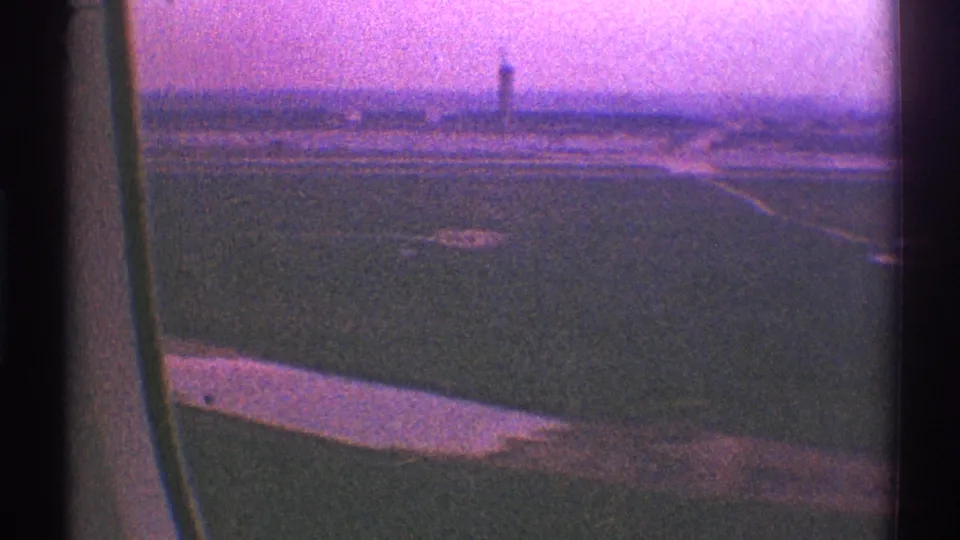 1969 passenger-window view of an airplane wing over Los Angeles airport grounds, with runway surfaces and a distant control tower.