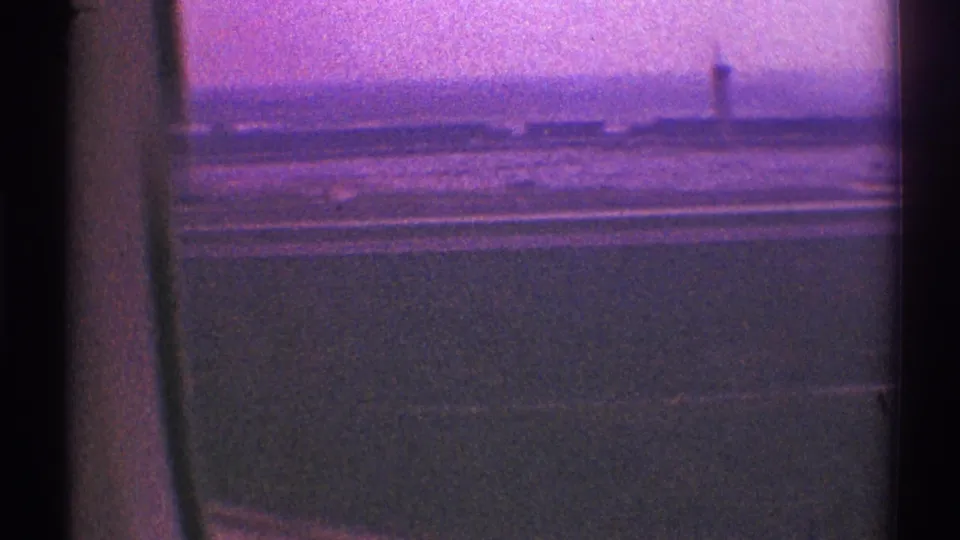Hazy 1969 Los Angeles aerial view with a dark window edge, open ground below, distant structures, and a tower on the horizon.