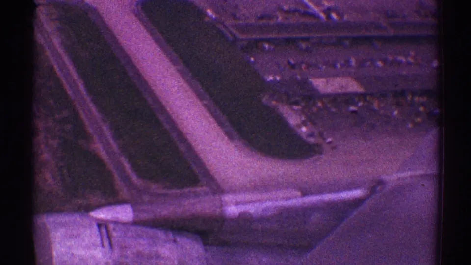 A passenger-window takeoff view shows the jet wing and engine crossing over runway or taxiway surfaces, airport grounds, and distant buildings in 1969 Los Angeles footage.