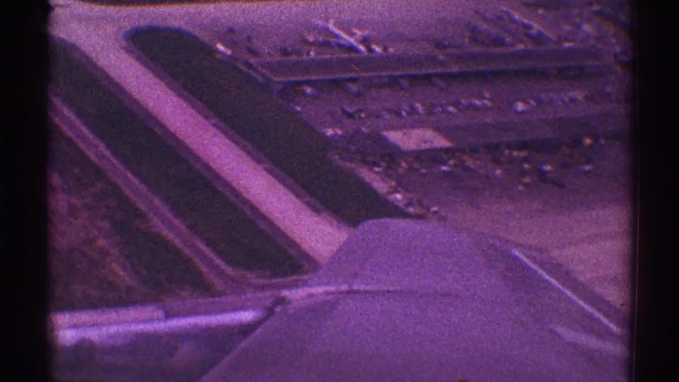 The plane continues to lift away, with the wing filling the lower frame and airport pavement, parked cars, and low buildings visible below in the Los Angeles takeoff view.