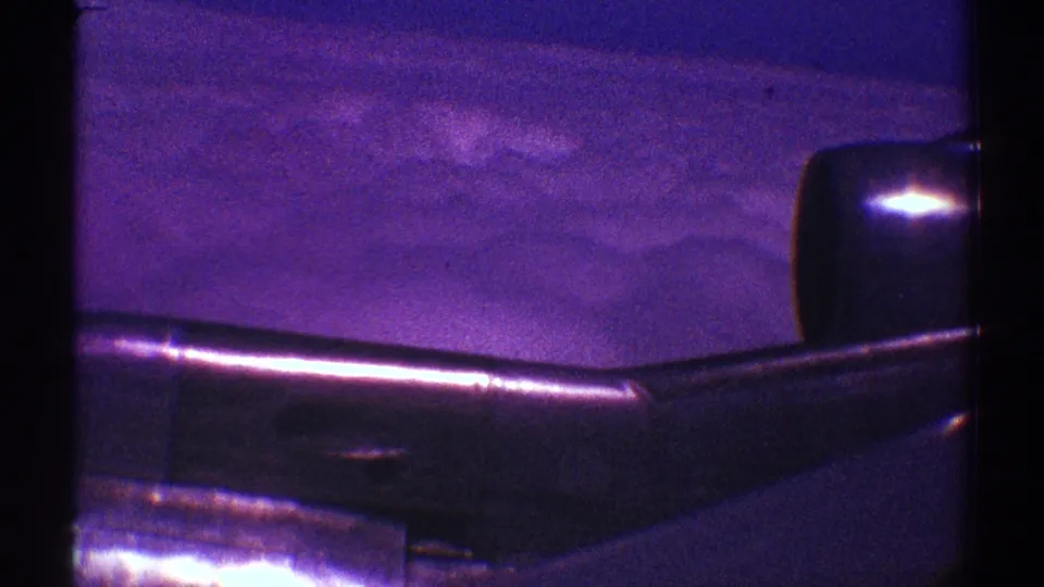 A 1969 Los Angeles passenger-window view showing the aircraft wing and engine with clouds beyond, tinted by aged 8mm film color.