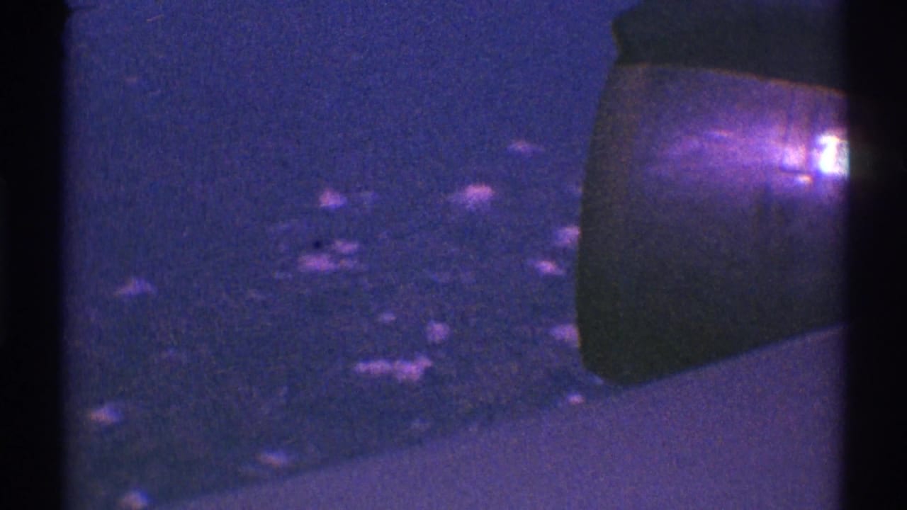 Dark purple-tinted view past a car mirror or body edge with scattered small light reflections below.