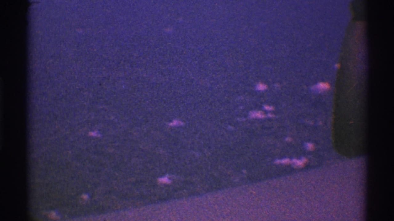 Dark purple aerial view through an airplane window with faint scattered lights and heavy film grain.