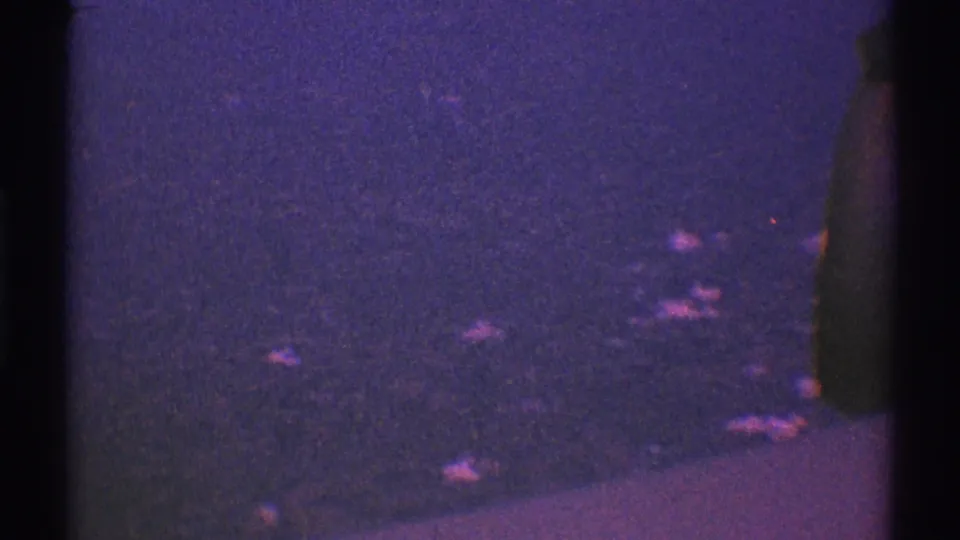1969 8mm aerial travel shot with a dark vertical window divider, purple grain, and indistinct lights below.