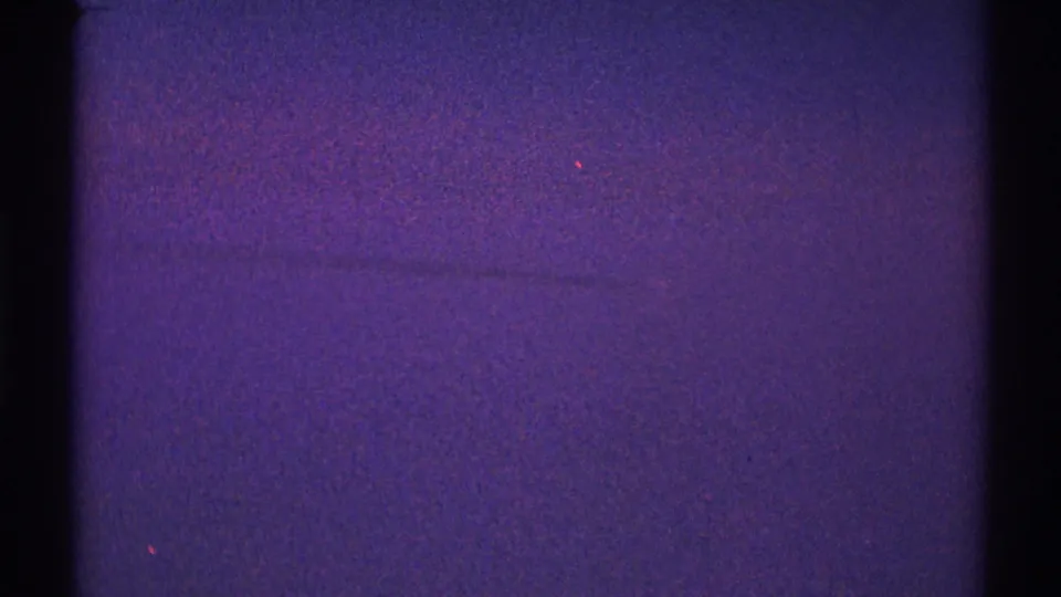 Purple-toned 8mm night-sky frame from the Los Angeles clip, with heavy grain, black borders, and a faint line in the sky.