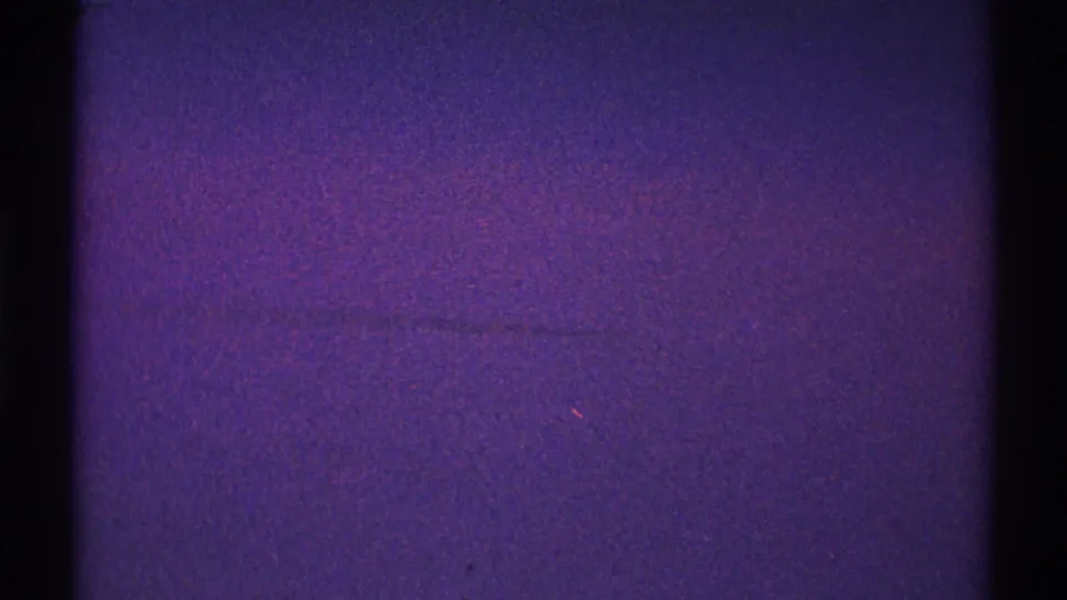 1969 Los Angeles 8mm night-sky frame with purple color shift, visible grain, black edges, and a few tiny light flecks.