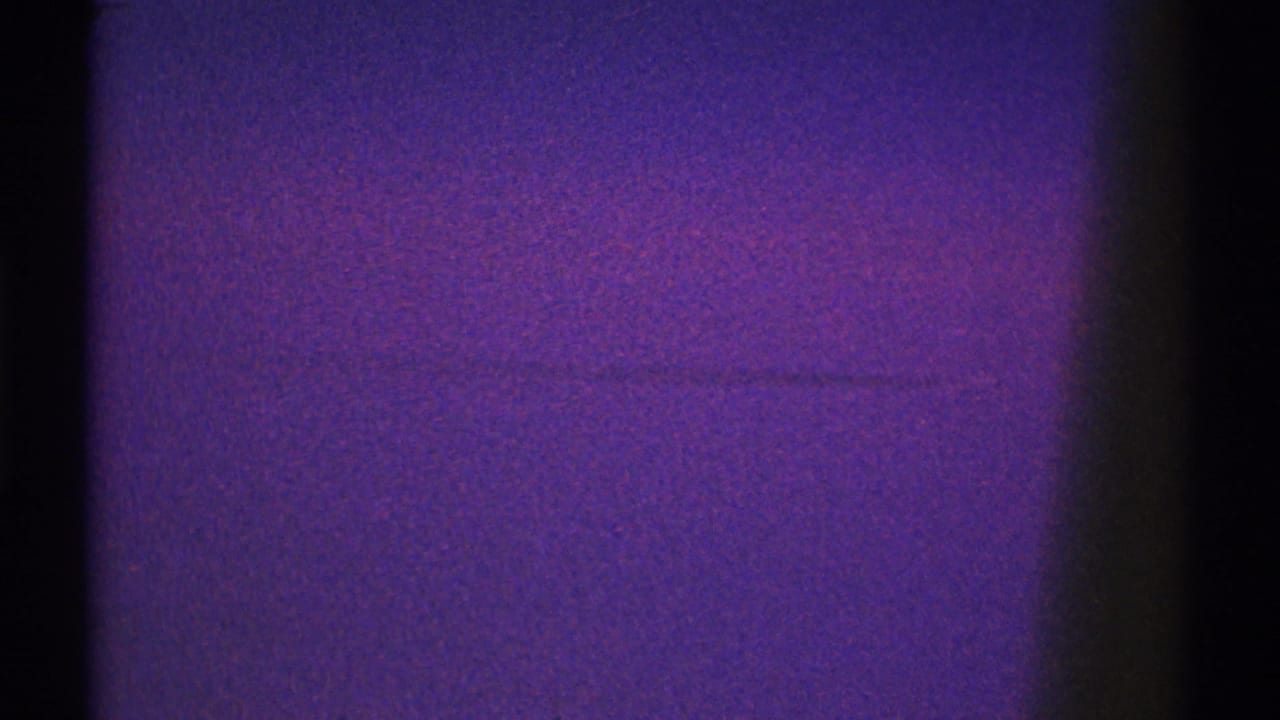 Purple-tinted dark frame with a faint horizontal streak and heavy film grain.