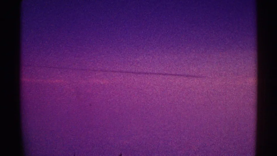 Grainy 1969 Los Angeles 8mm frame showing a purple-toned sky or window view with a faint horizontal line.