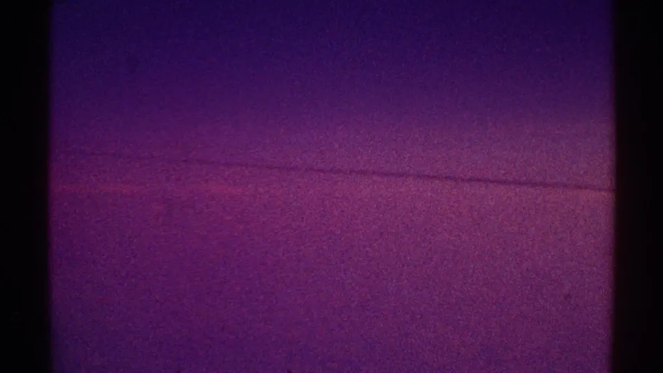 1969 Los Angeles 8mm frame showing a dim streak low in a purple night sky with pronounced grain and gate shadow.