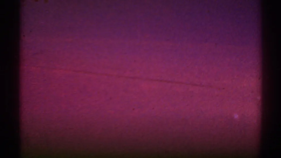 1969 8mm frame from the Los Angeles clip showing a reddish exposure or leader-like moment before the aerial farmland view becomes clear.