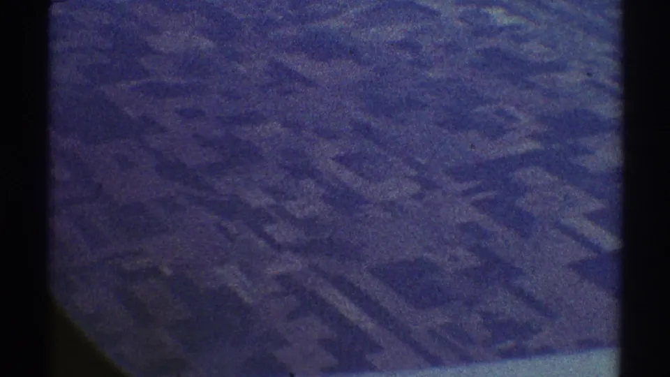1969 Los Angeles-area aerial view showing geometric agricultural plots below, softened by aged 8mm grain and a blue-purple color cast.