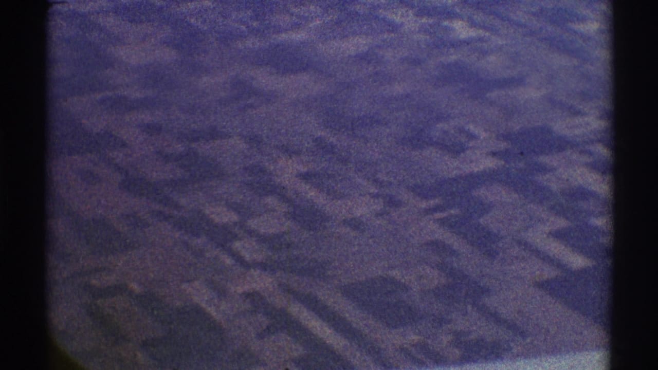 1969 8mm aerial view over indistinct patterned terrain in the Los Angeles area, tinted blue-purple with visible grain.
