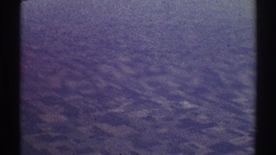 Grainy 1969 8mm aerial frame with indistinct terrain, faded purple color, and a visible horizontal exposure change.
