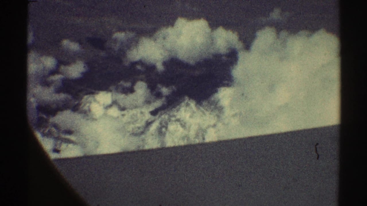 Snowy mountain peaks partly hidden by clouds, seen through dark film-frame edges.