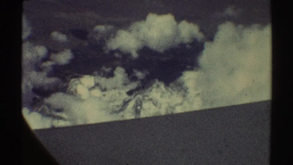 1969 8mm aerial view of snowy mountain ridges beneath dark cloud cover, with visible frame borders and grain.
