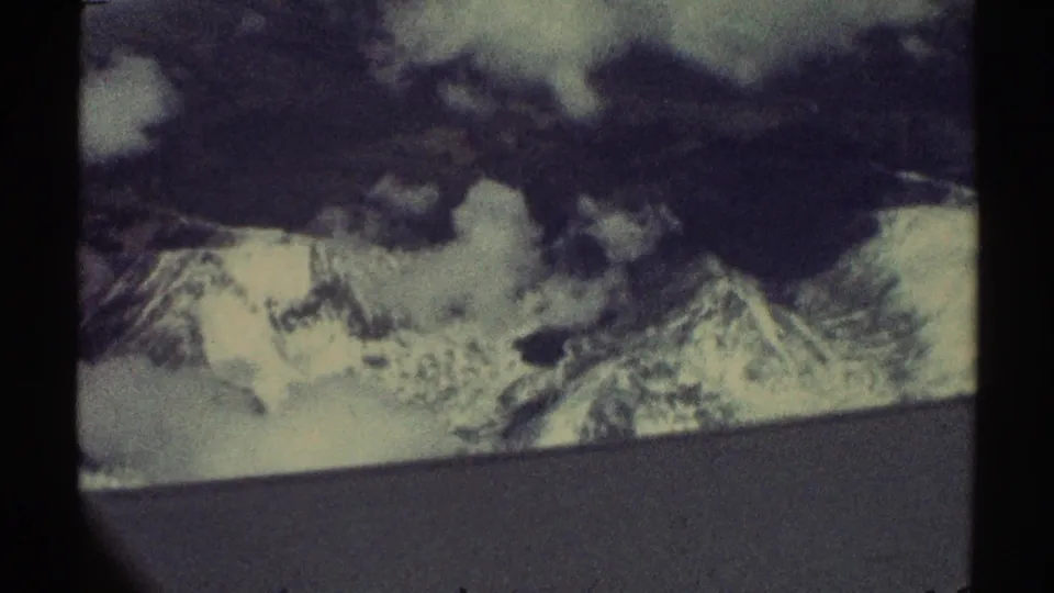 1969 8mm aerial home-movie view of snow-covered mountain peaks broken by heavy clouds and visible film borders.