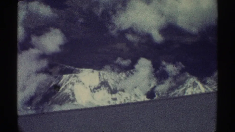 1969 8mm aerial travel frame with cloud banks passing over a snow-covered mountain range from a passenger viewpoint.